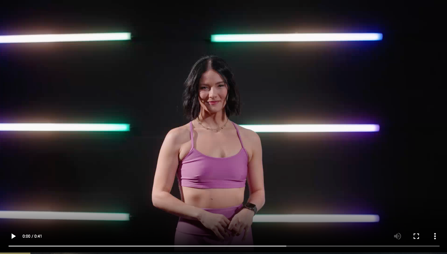 Woman in purple top, talking about the reformer in a dark studio